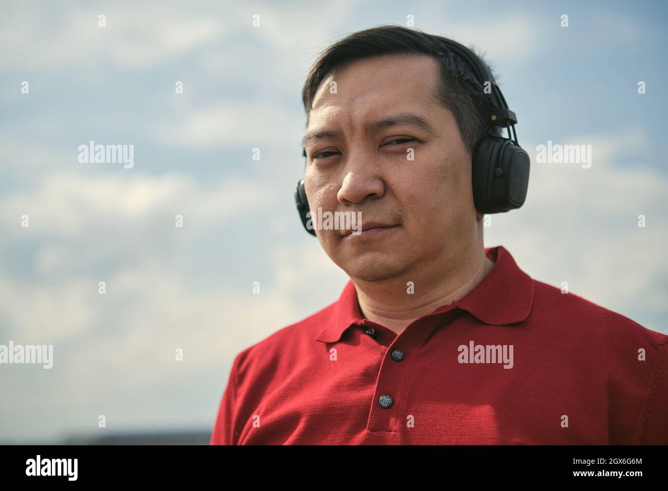 Middle-aged Asian man in headphones outdoors listening to music against the background of the sky Stock Photo