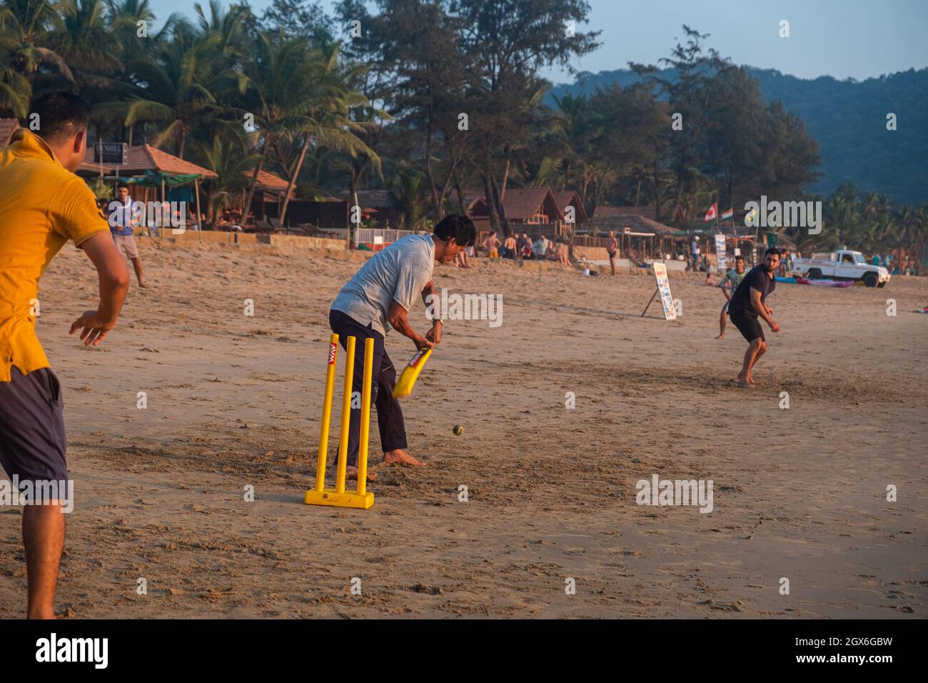 Group of Indian adults playing cricket on beach at sunset, Goa, India Stock Photo