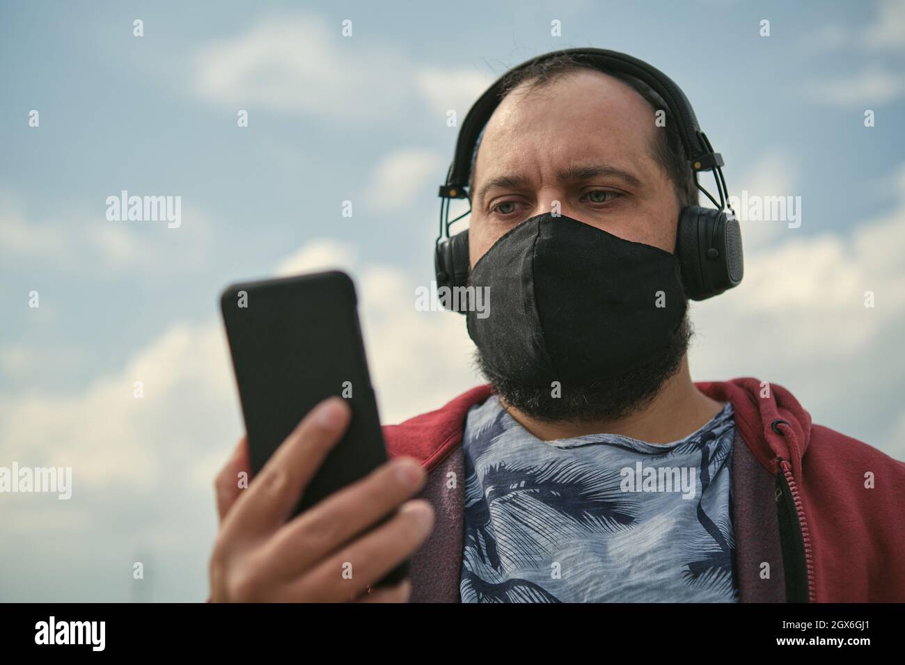Middle-aged European man in headphones outdoors listening to music against the background of the sky, mobile phone in his hand Stock Photo