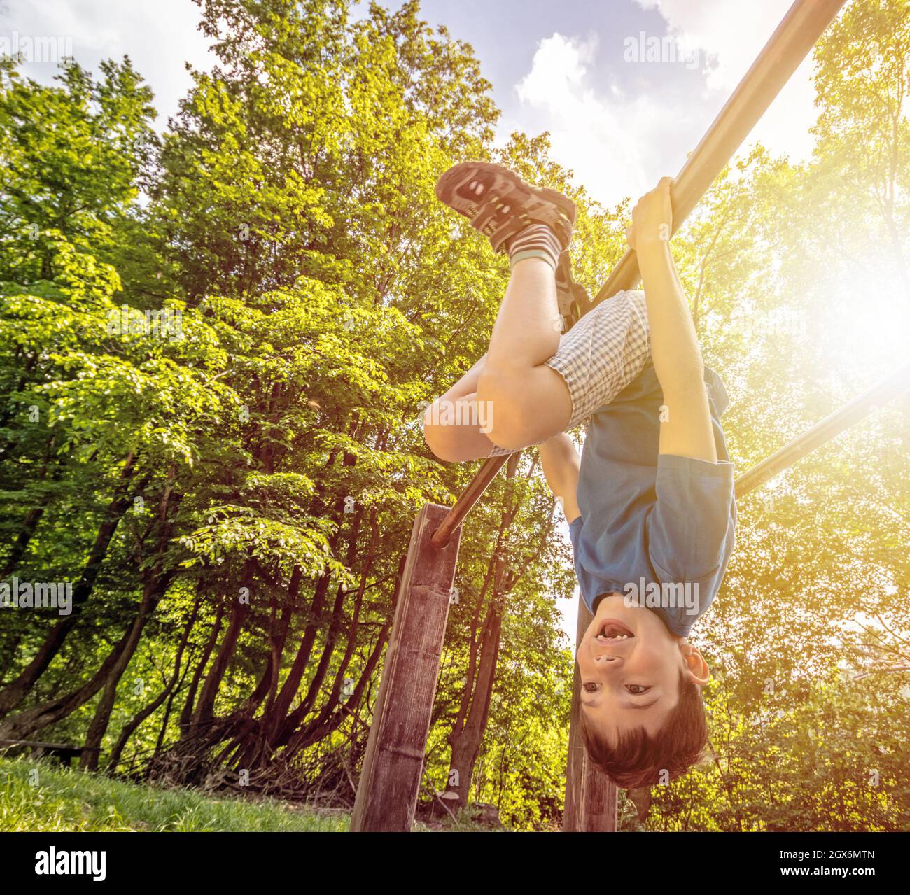 Happy child boy hanging upside  down on bar, playground in forest, outdoor activities Stock Photo