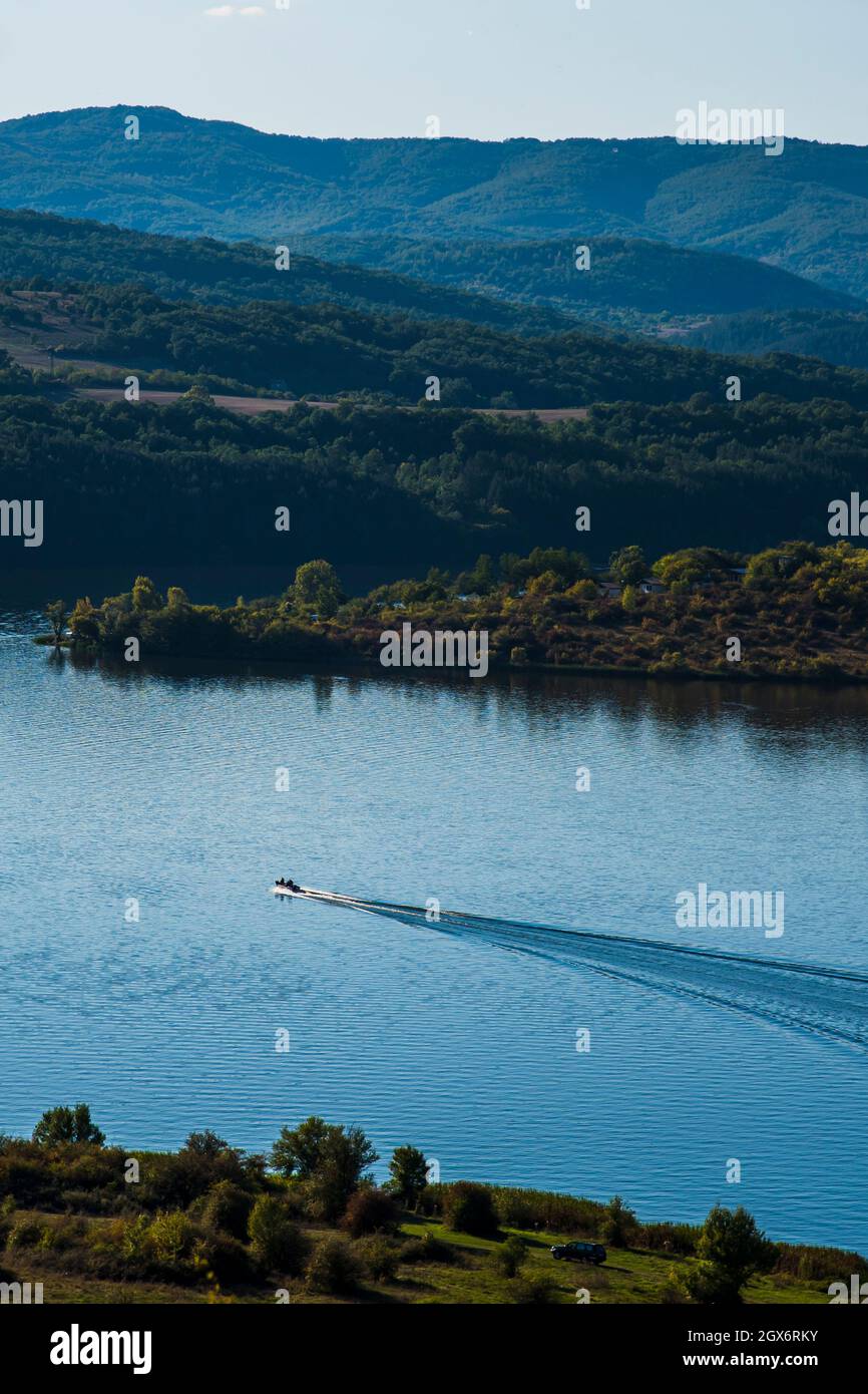 A boat speeding through a lake. A lake, sea, coast between mountains, rocks, nature in Bulgaria. Beautiful sunny day Stock Photo