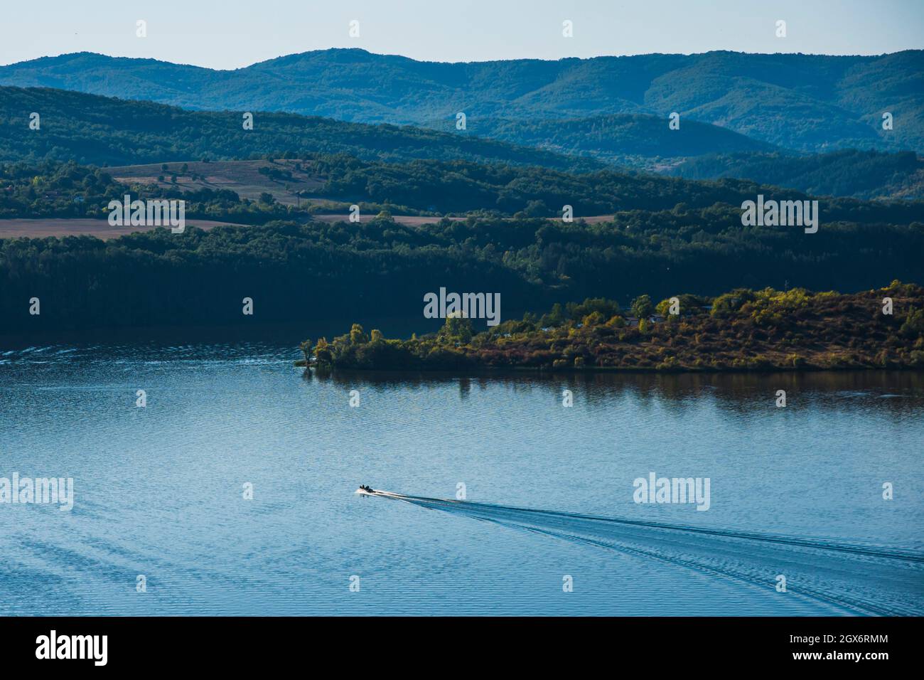 A boat speeding through a lake. A lake, sea, coast between mountains, rocks, nature in Bulgaria. Beautiful sunny day Stock Photo