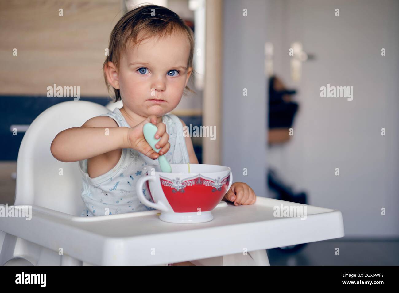 half-length view of a adorable blue-eyed little girl eats soup from the bowl and looks at the camera Stock Photo