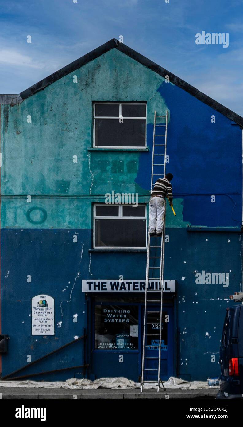 Painting the building blue. A man on a ladder painting a building a deep shade of blue. Stock Photo