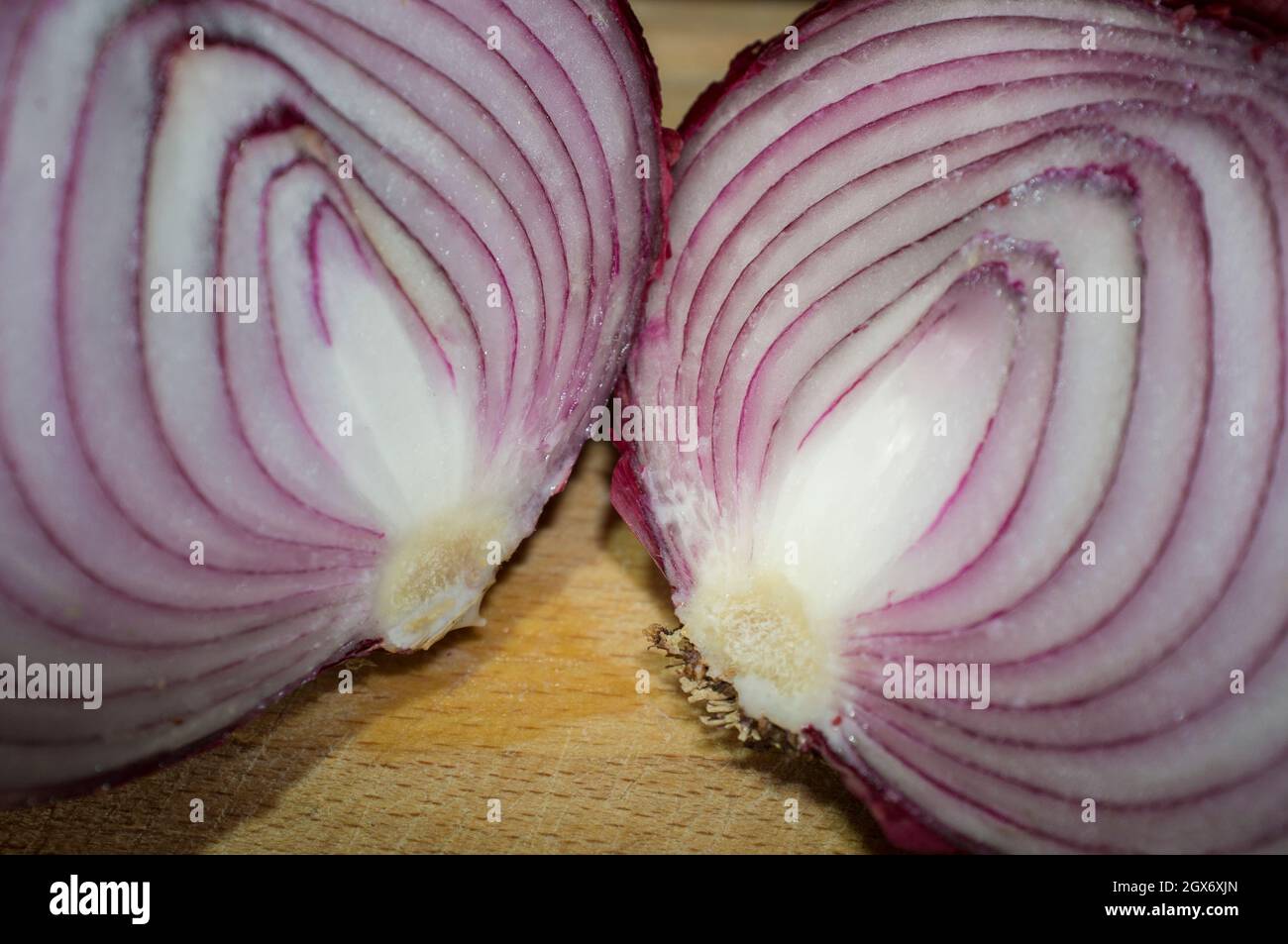 Cross sections of raw red onions. Closeup over wooden cutting board Stock Photo