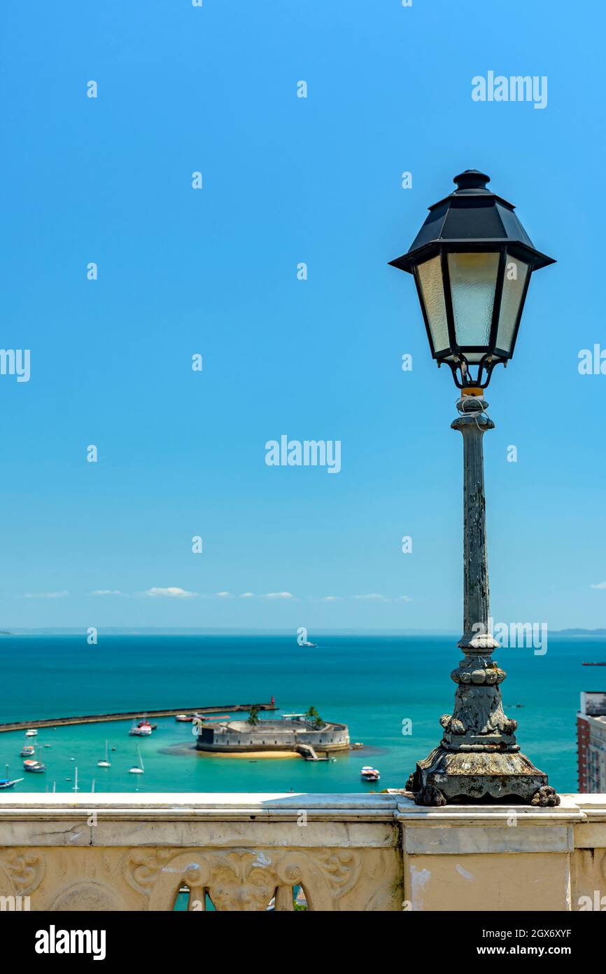 Old lamppost on a wall overlooking the sea and historic fortification in Todos os Santos Bay in Salvador, Bahia Todos os Santos Bay in Salvador, Bahia Stock Photo