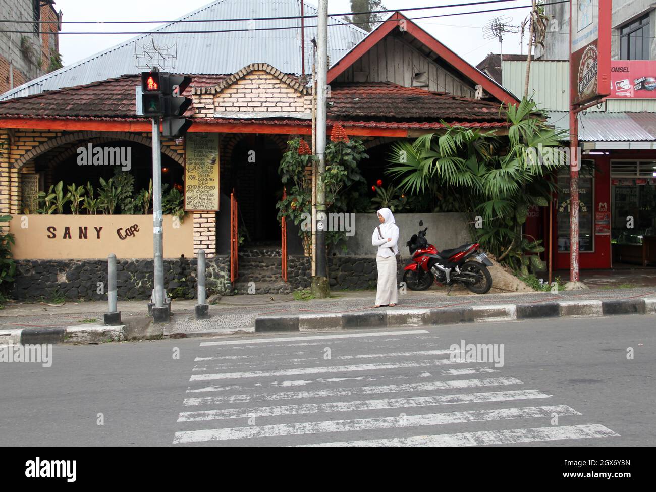A young woman dressed in white and wearing a white hijab is waiting to cross a road in front of the Sani Cafe in Bukittinggi, West Sumatra, Indonesia. Stock Photo