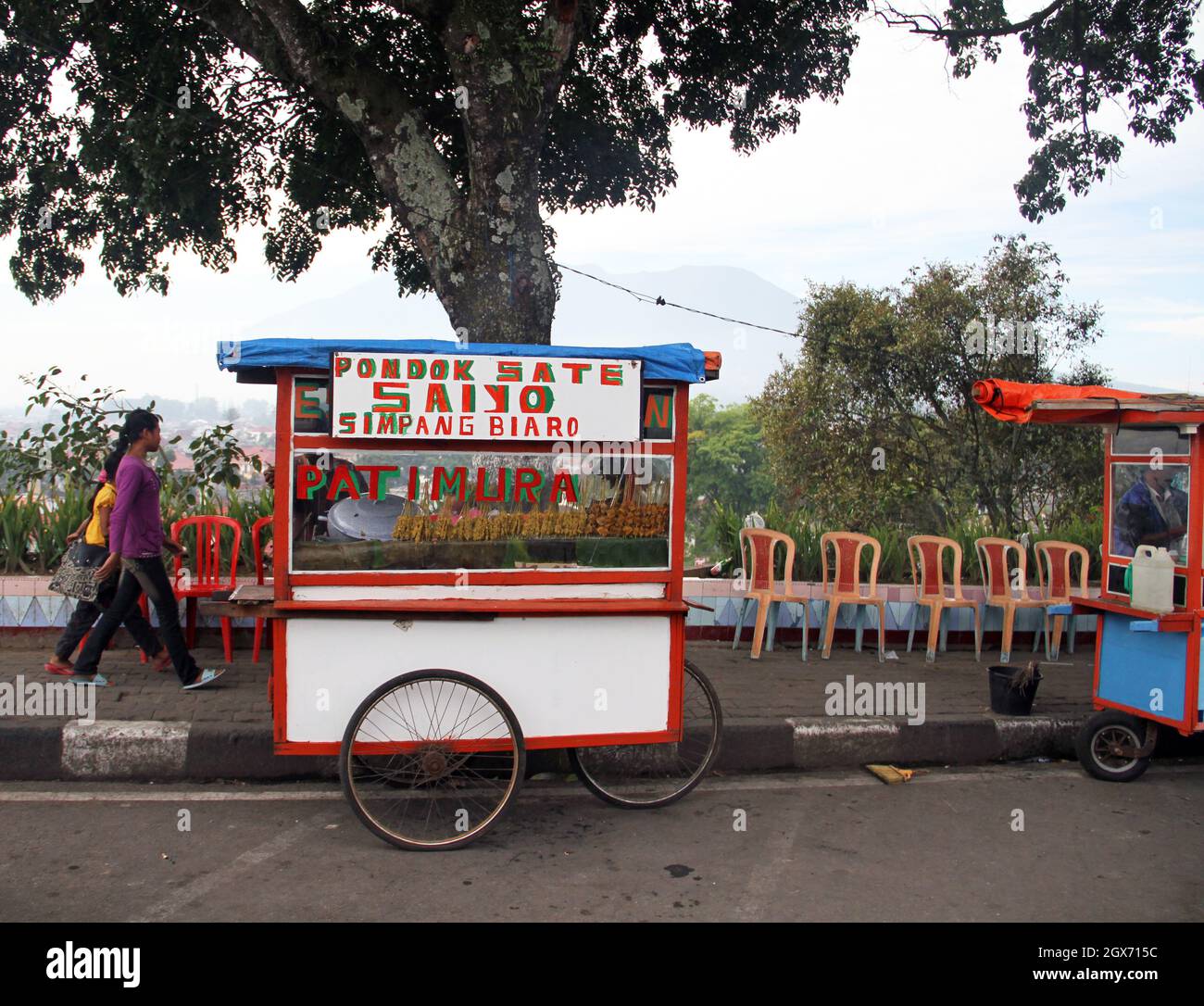 A street food vendor of chicken and goat meat sate or satay with food cart and two children playing behind, in Bukittinggi, West Sumatra, Indonesia. Stock Photo