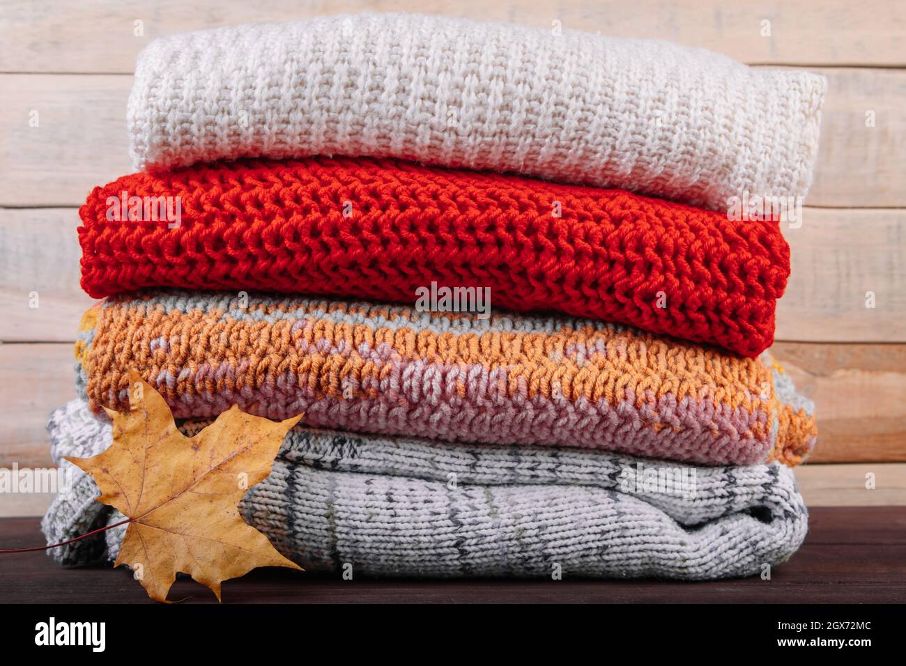Stack of warm knitted sweaters. Autumn concept. Woolen jumpers and maple leaf on a wooden background. Stock Photo