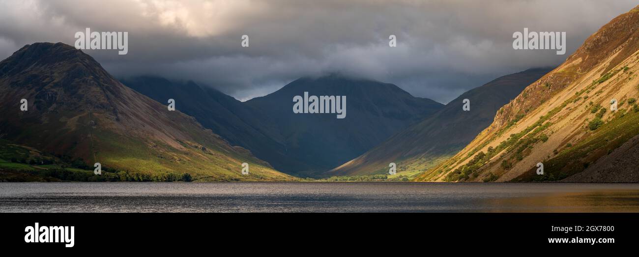 A fleeting patch of light highlights the dramatic screes bordering Wastwater with the mountains at the head of the valley shrouded in darkness. Stock Photo