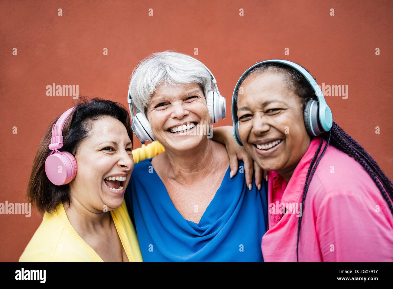 Multiracial senior woman having fun listening playlist music with headphones together - Elderly lifestyle concept - Focus on center woman face Stock Photo