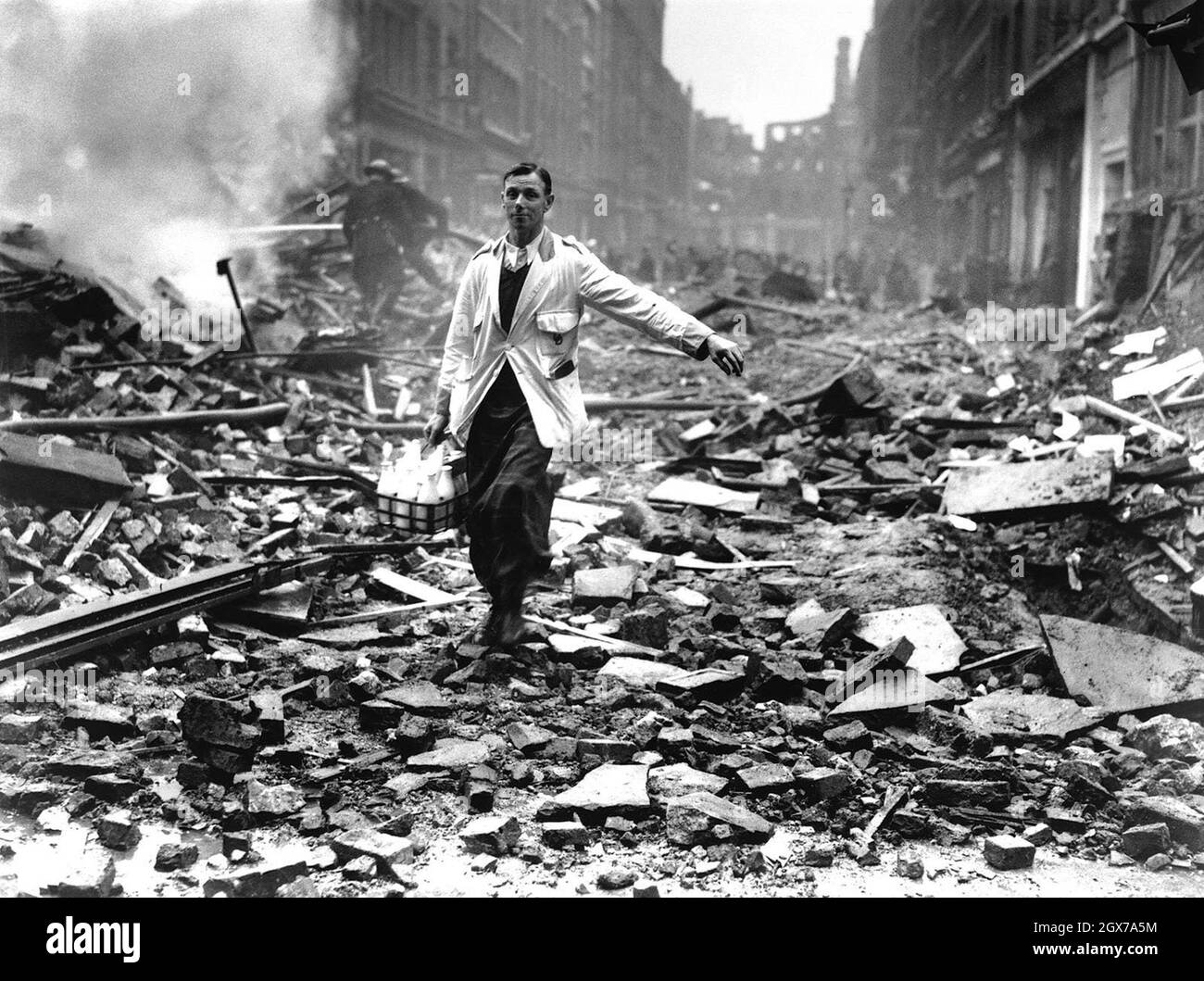 A London milkman delivering milk to homes, walking acrossa rubble filled street, showing Business As Usual Stock Photo