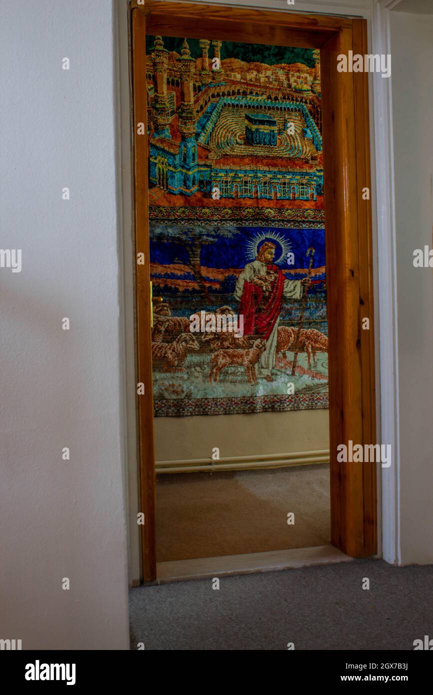 Jesus and Kaaba wall carpet on the wall looking through doorframe. Religious wall accesories. Stock Photo