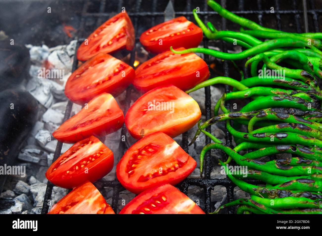 Thin green peppers and tomatoes on charcoal grill. Black grill marks