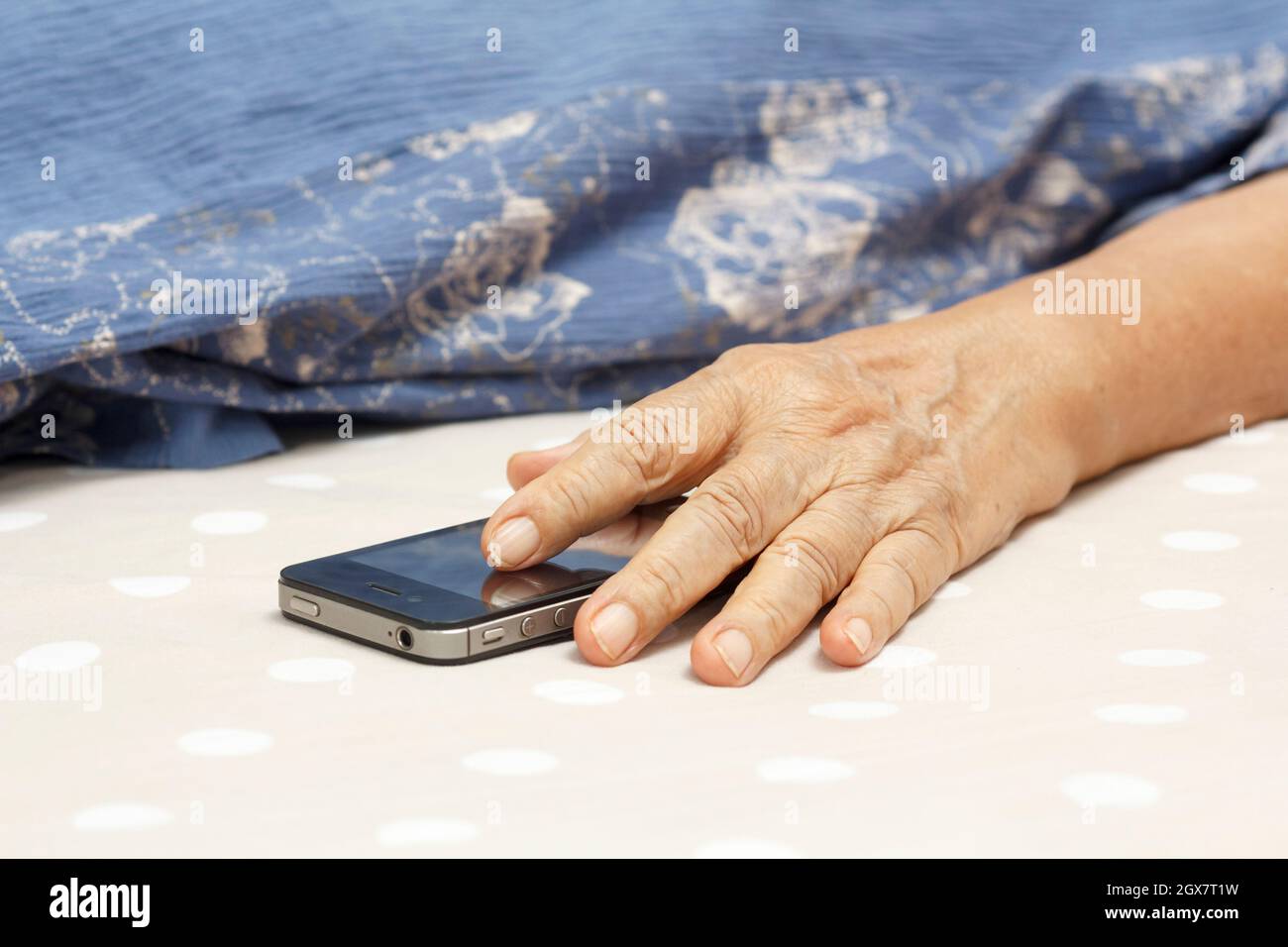 Elderly woman sleeping in bed and holding a mobile phone. Stock Photo