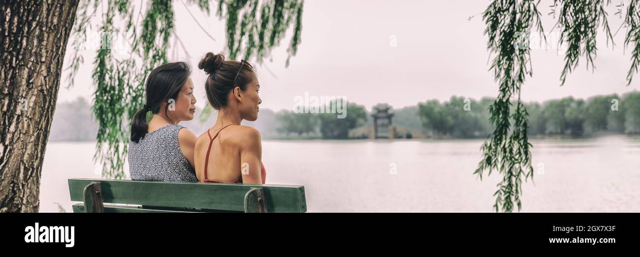 Mom and daughter happy relaxing together at Beijing summer palace lake park enjoying quiet summer day traveling in China. Two women relaxing peaceful Stock Photo