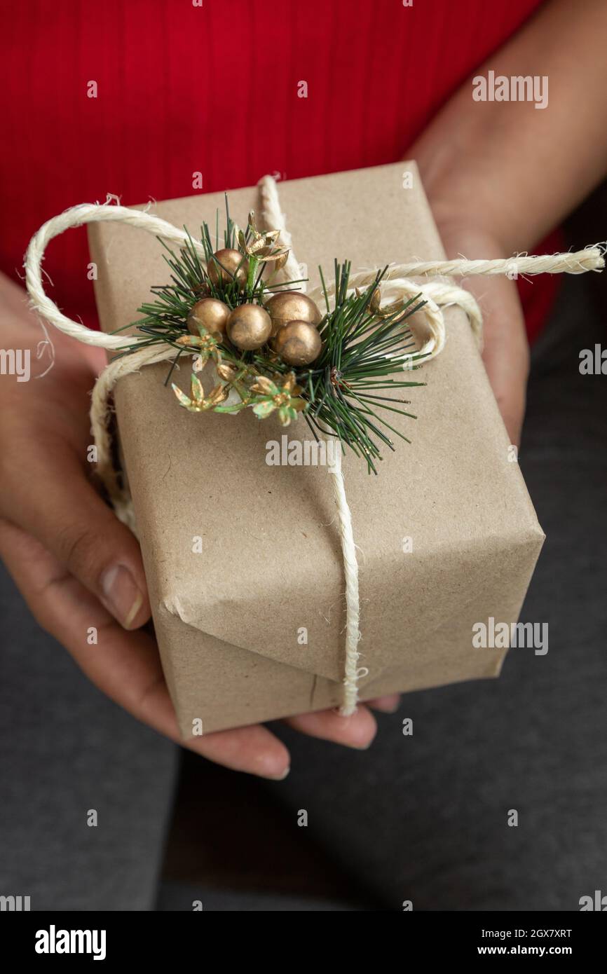 hands of a person with a gift decorated cream paper, ribbon, christmas ornament and cinnamon stick, share details at christmas, lifestyle that brings Stock Photo