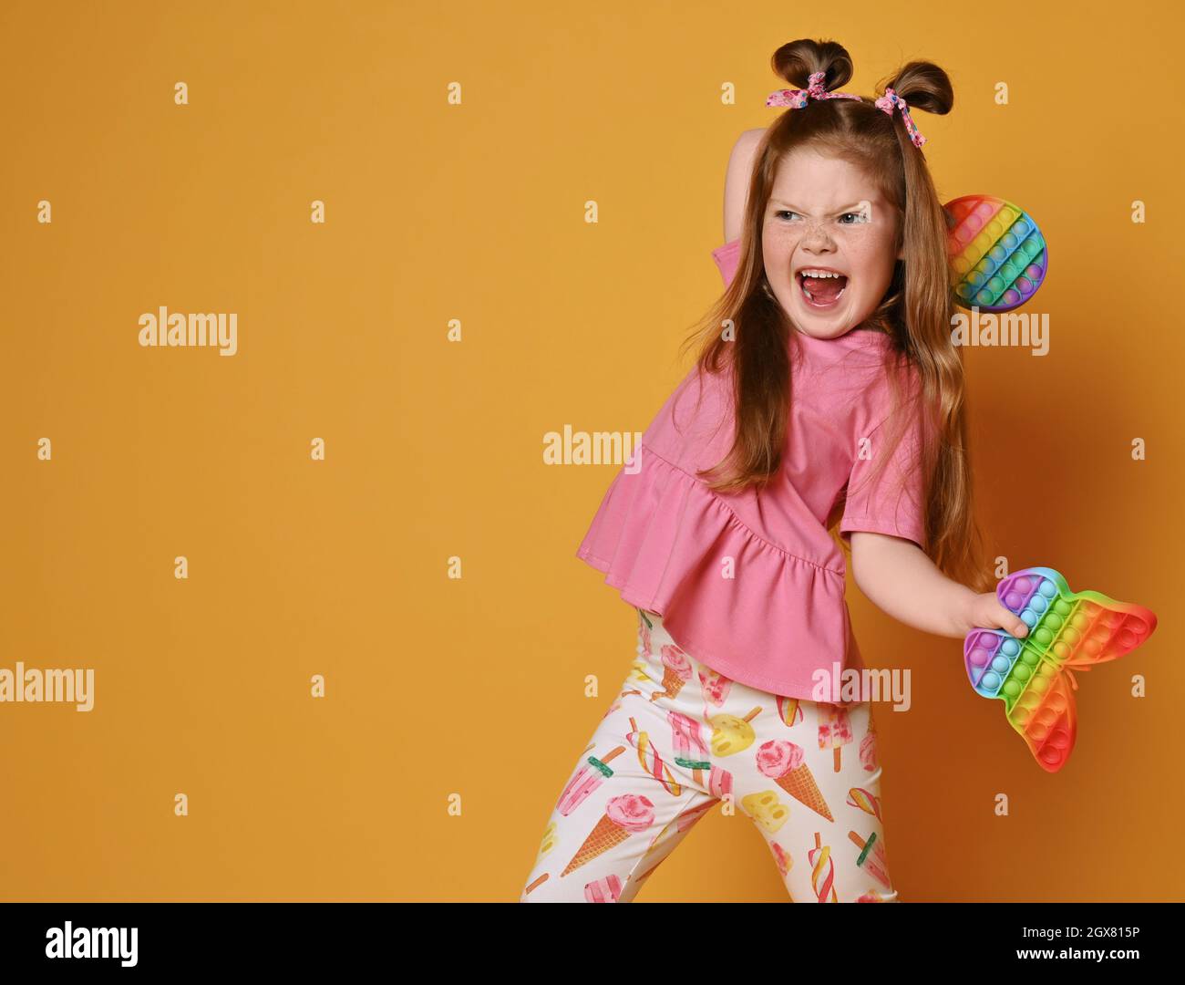Frolic, screaming, spoiled kid girl in colorful clothes going to throw two sensory rainbow color toys - round pop Stock Photo