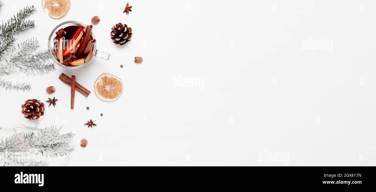 Christmas banner flat lay on white gray background with glass cup or mug of Mulled Wine, present red gift box, decorations, cinnamon, orange, apple, v Stock Photo