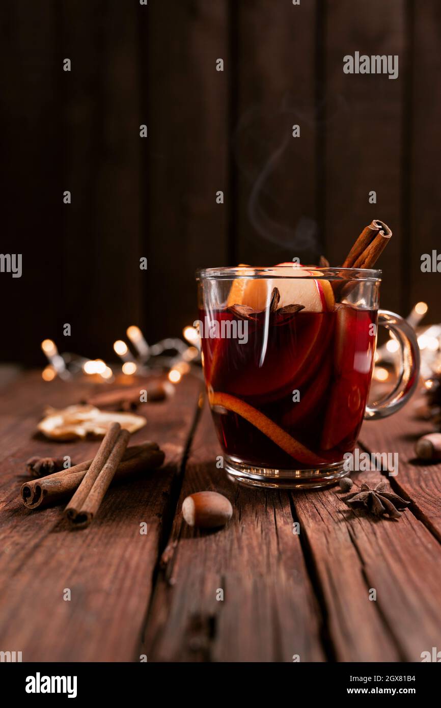 Christmas time concept photo. Glass cup or mug with Mulled Wine inside on wooden table and background. Garlands, decorations, cinnamon, hazelnut, drie Stock Photo
