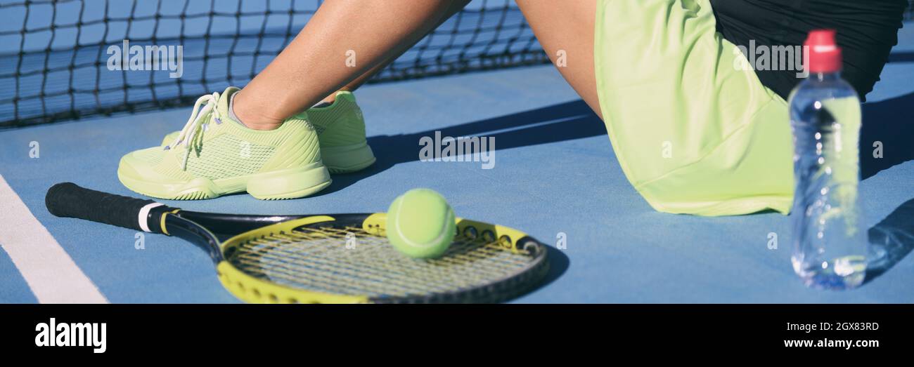 Tennis athlete player woman wearing tennis shoes yellow activewear outfit with racket and water bottle on blue outdoor hard court panoramic banner Stock Photo