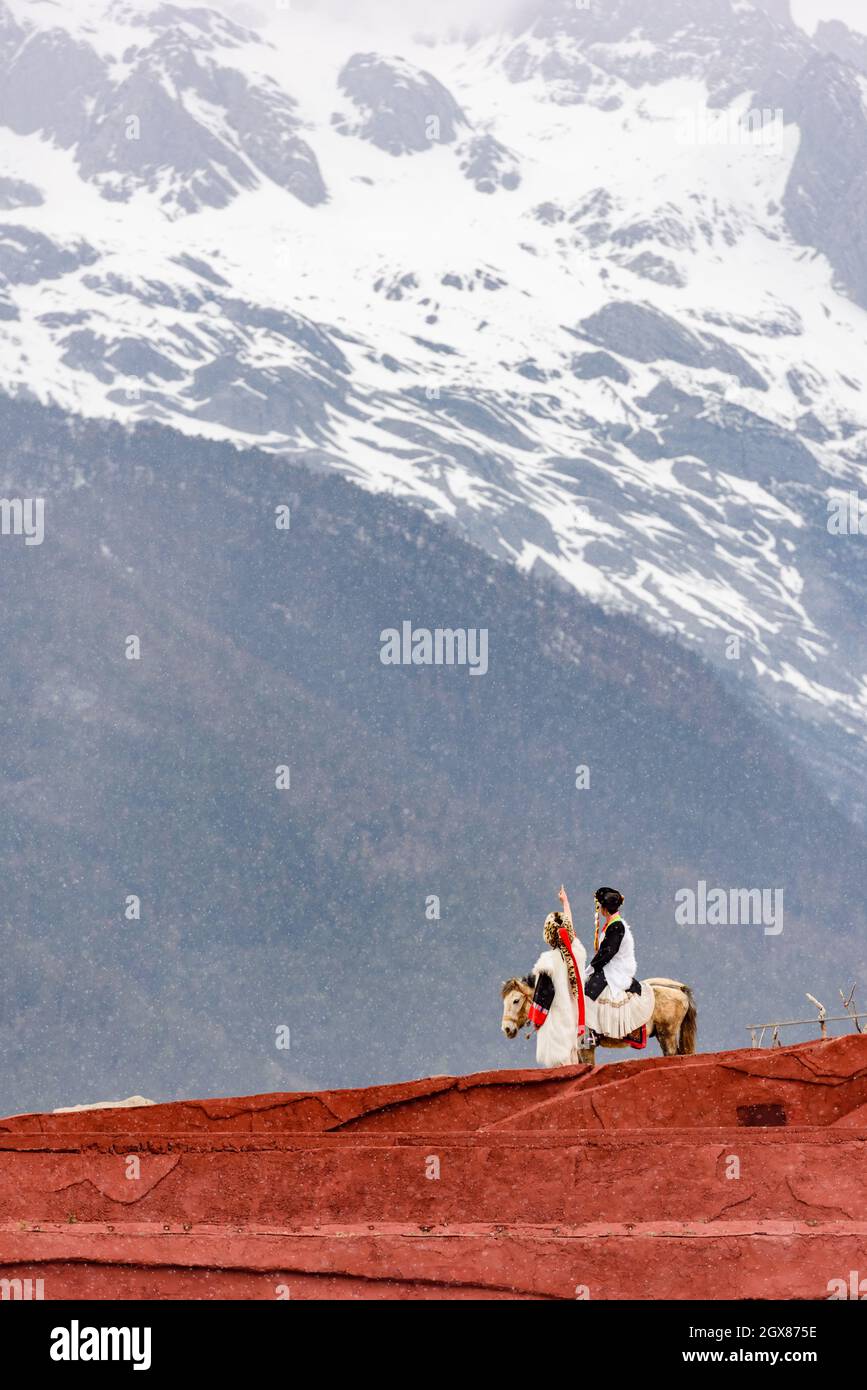 Couple riding horse pointing at Yulong snow mountain, Yunnan, China. Stock Photo