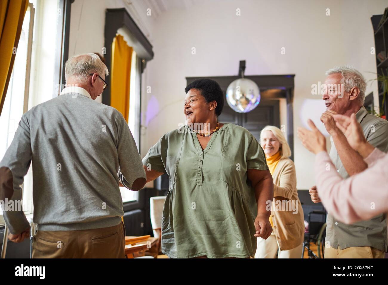 Diverse group of smiling senior people dancing while enjoying activities in retirement home, copy space Stock Photo