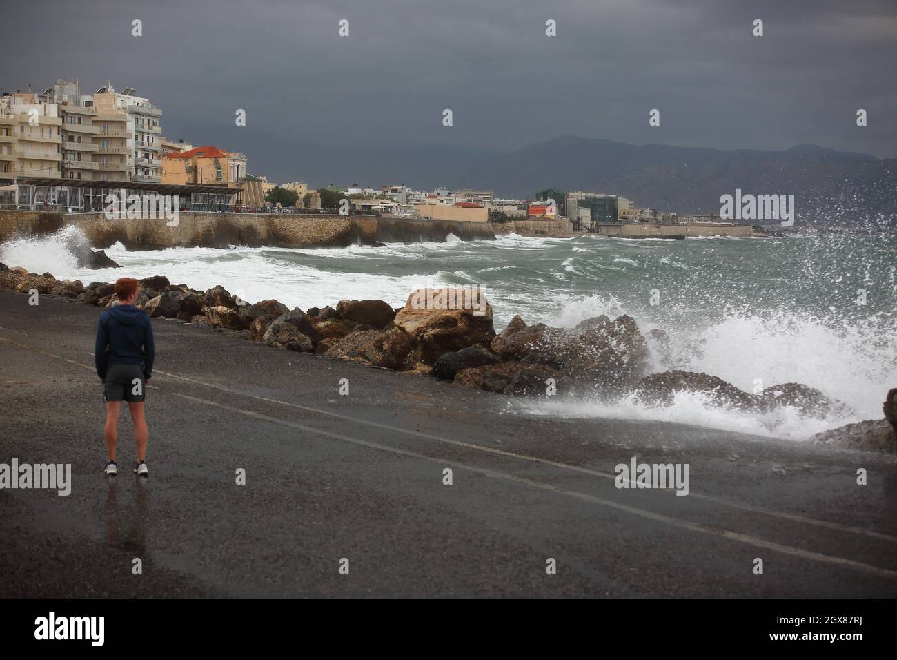 Lonely man stands on shore watching splashing waves on stones rocks on embankment, Heraklion, Crete, rainstorm, waes on sea Stock Photo