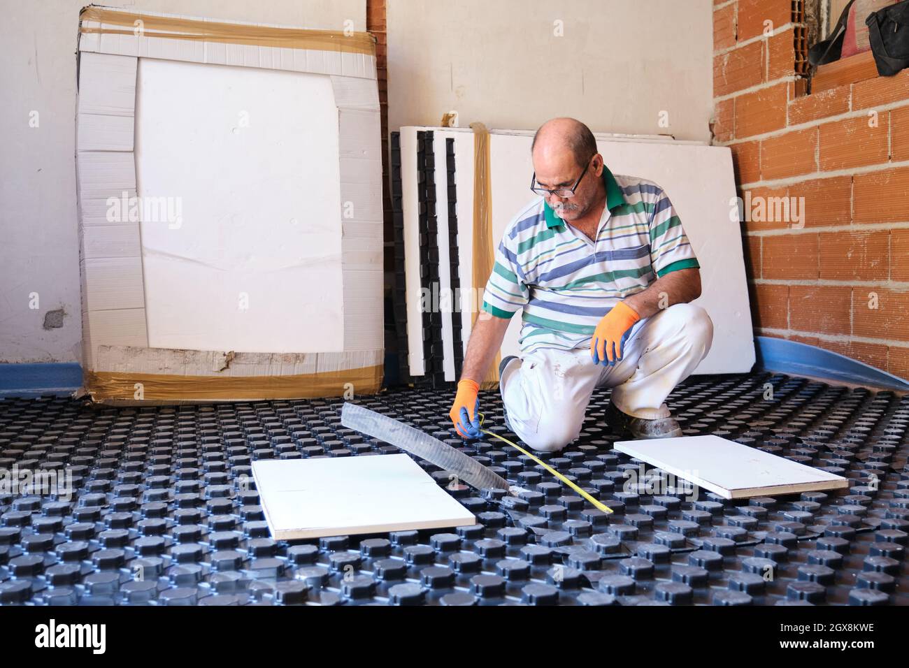 Worker measuring with tape before installing radiant floor system. Stock Photo