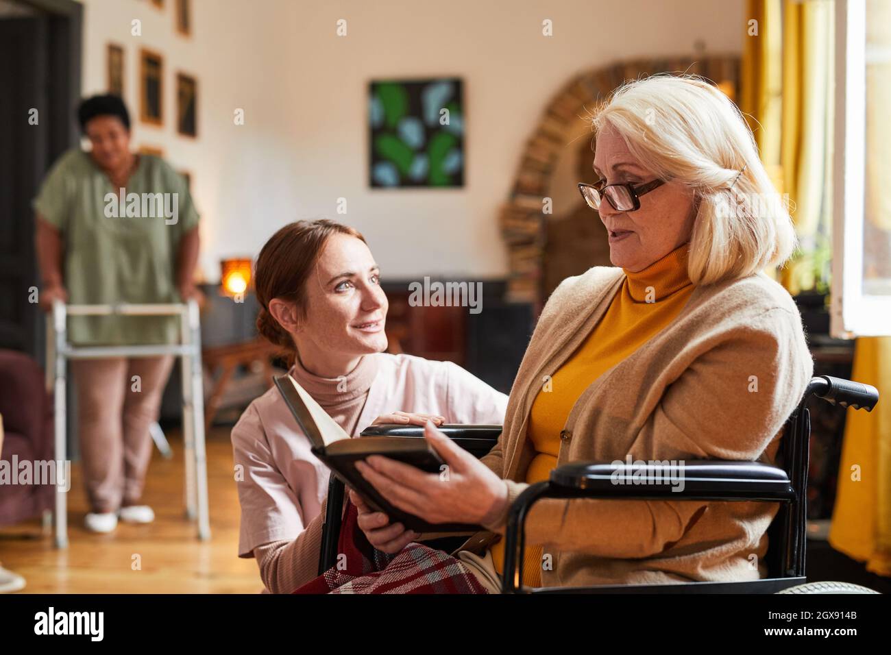 Portrait of young woman assisting senior woman in wheelchair at retirement home, copy space Stock Photo