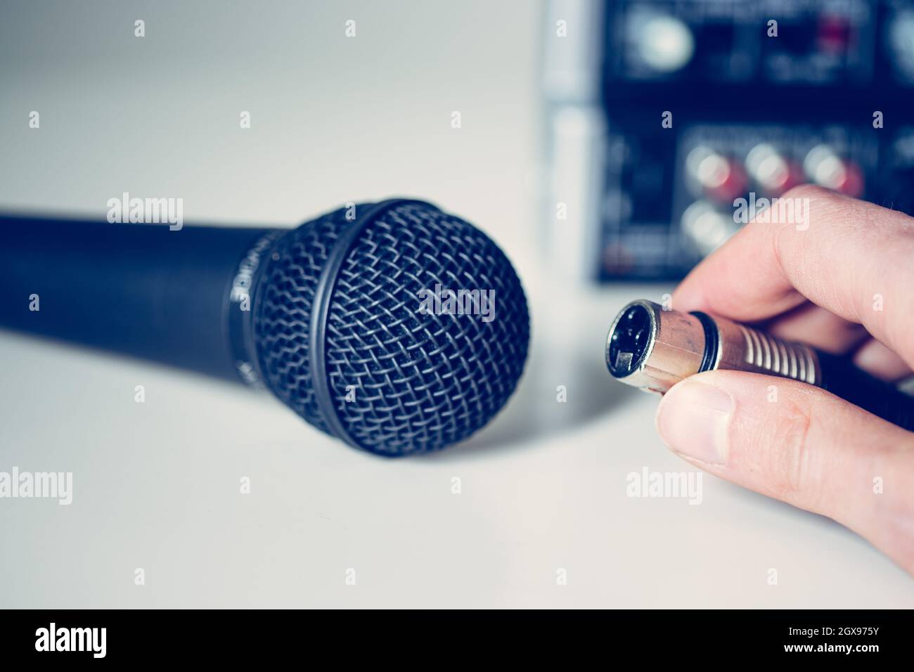 Close up picture of holding in hand microphone and audio cable, mixer in the blurry background Stock Photo