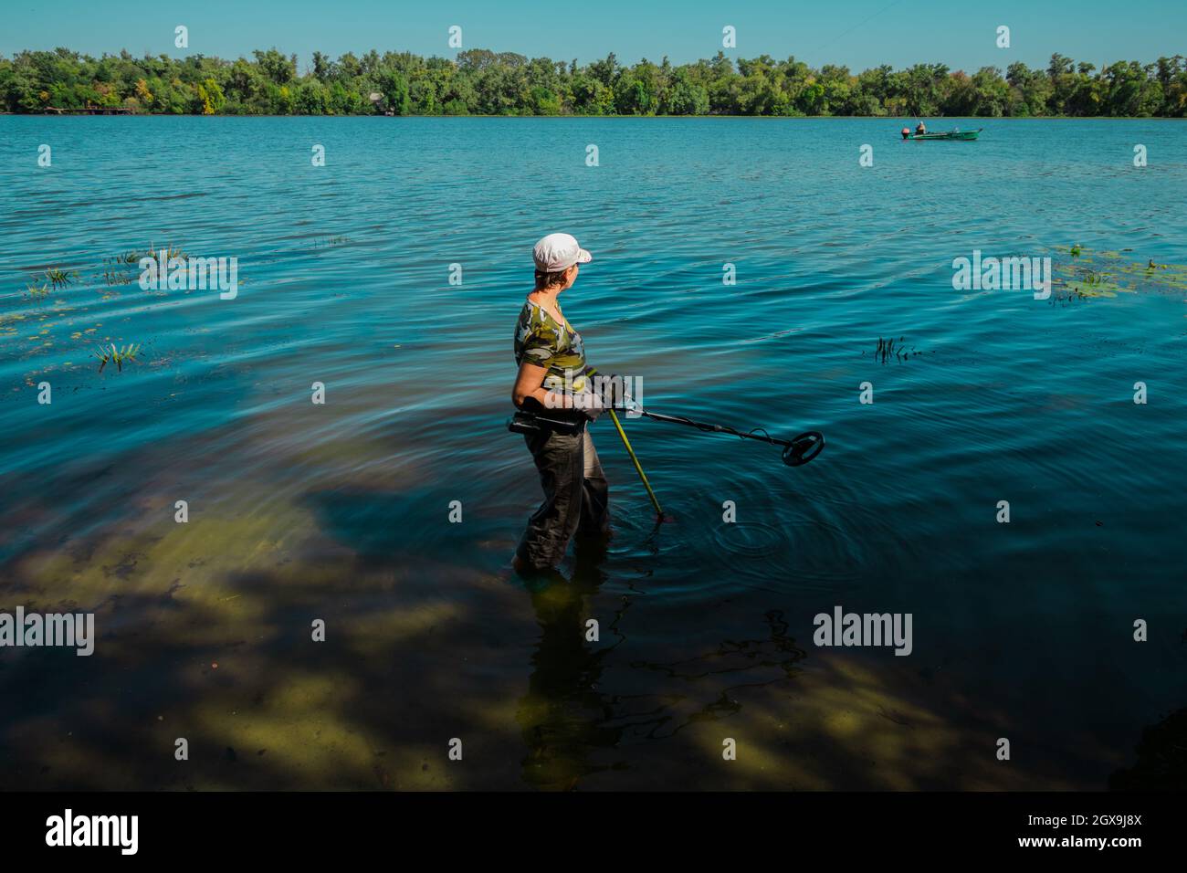 A woman searches for treasures in the water using a metal detector.  Stock Photo