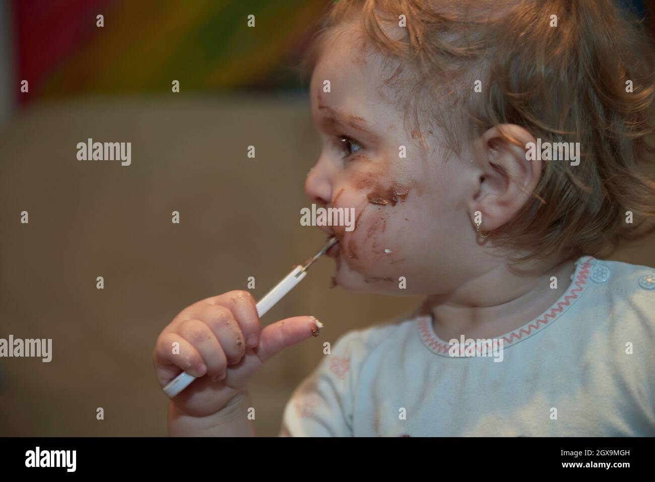 Cute little baby girl eating her chocolate desert after dinner with a spoon and making a mess dirty face Stock Photo