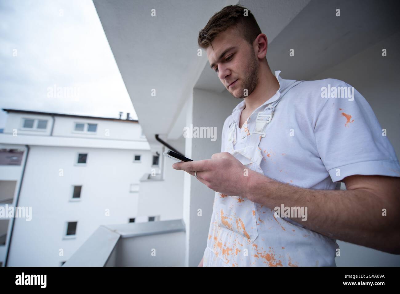 Painter making telephone call while standing on balcony during break from work  Decorator Using Mobile Phone Standing Outside Stock Photo