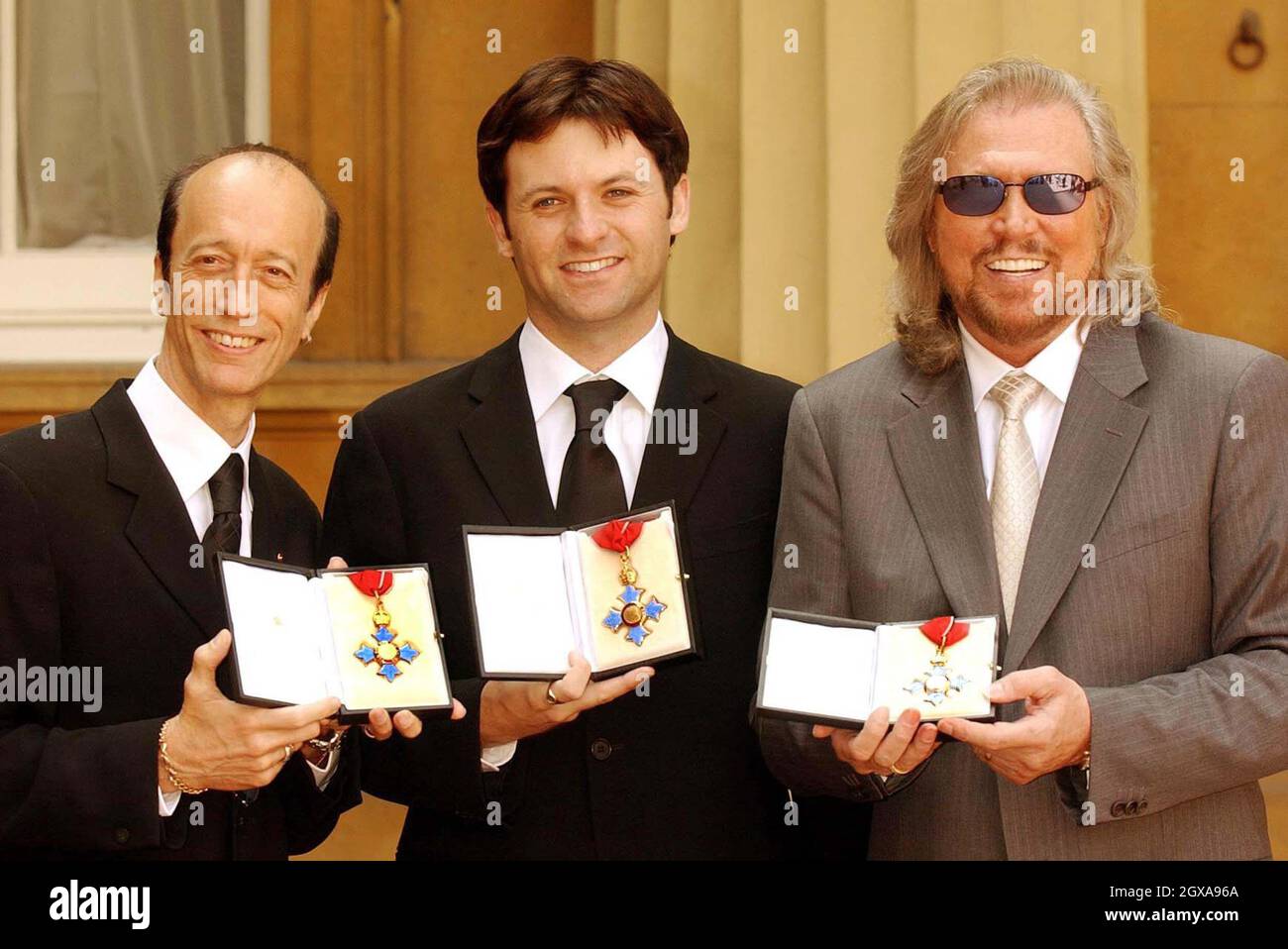 The two surviving members of the Bee Gees, Robin Gibb (left) and Barry Gibb (right) hold their CBE's along with Adam Gibb who received the honour on behalf of his father, the late Maurice Gibb, at Buckingham Palace, London, Thursday May 27, 2004. All three brothers were awarded CBE's although Maurice Gibb died last year before he could receive the honour  Stock Photo