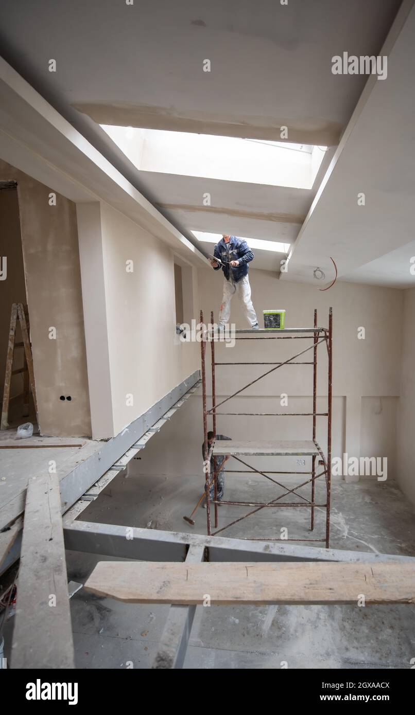 https://c8.alamy.com/comp/2GXAACX/young-professional-construction-worker-using-scaffold-while-plastering-on-gypsum-ceiling-inside-the-new-big-modern-two-levels-apartment-2GXAACX.jpg