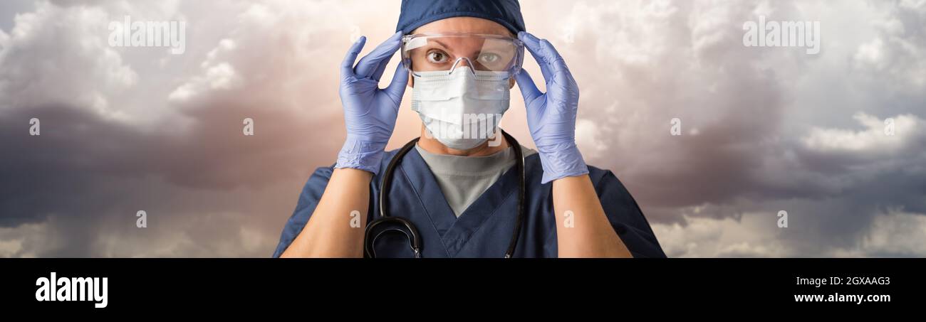 Doctor or Nurse Adjusting Safety Goggles Wearing Personal Protective Equipment Over Ominous Clouds. Stock Photo
