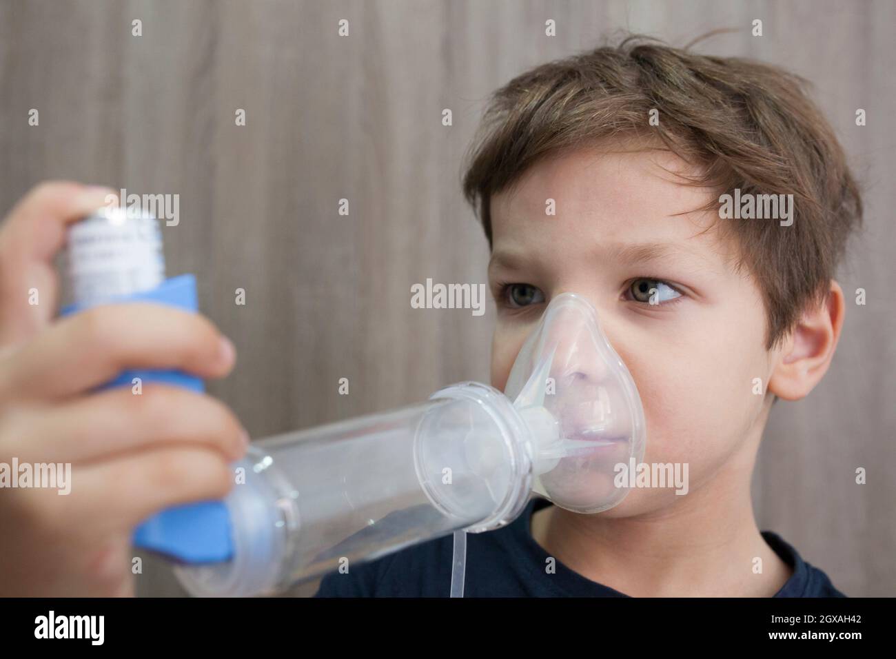 Child boy using medical spray for breath. Inhaler, spacer and mask. Side view. Stock Photo