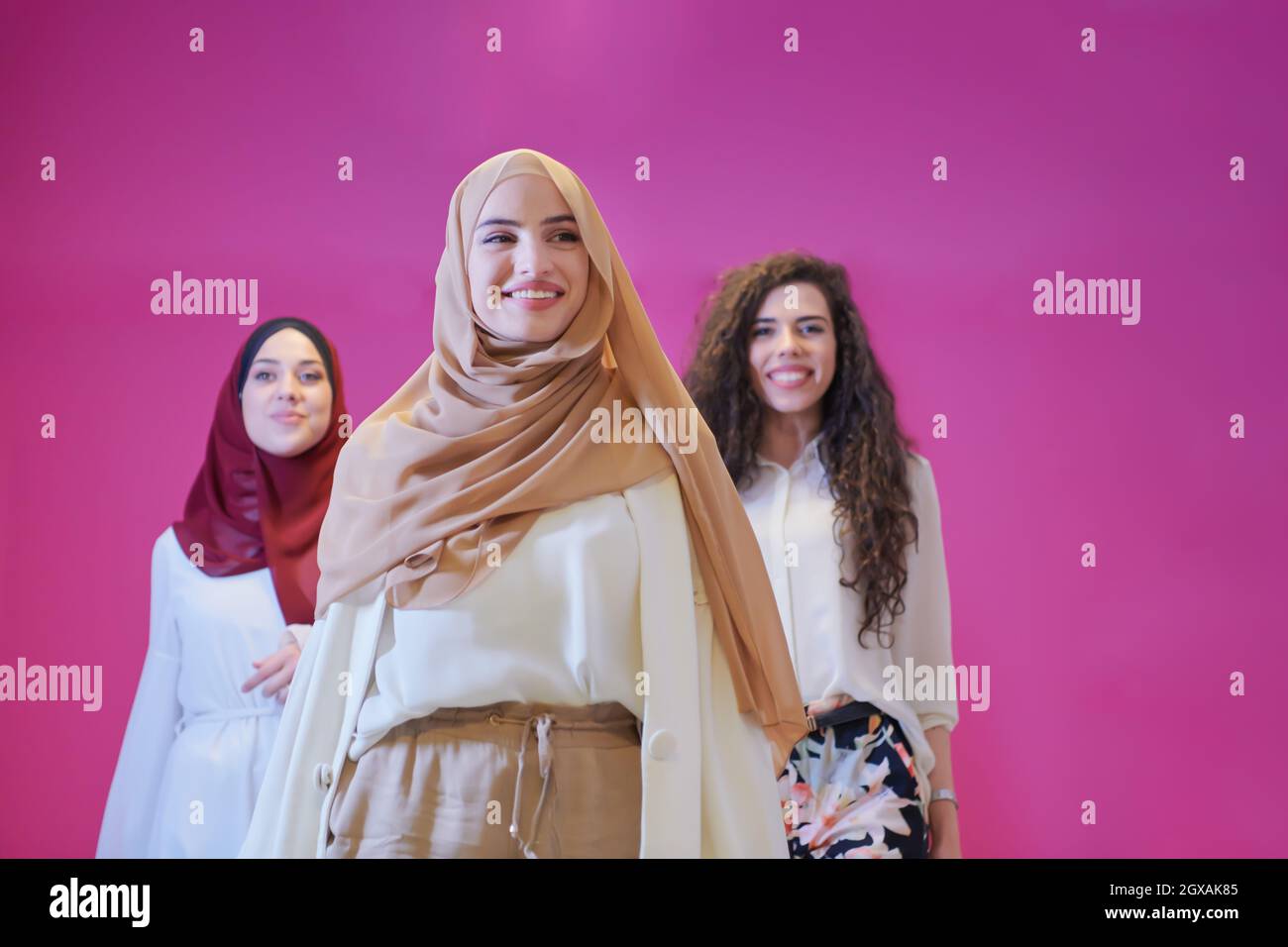 group portrait of beautiful muslim women two of them in fashionable dress with hijab isolated on pink background representing modern islam fashion and Stock Photo