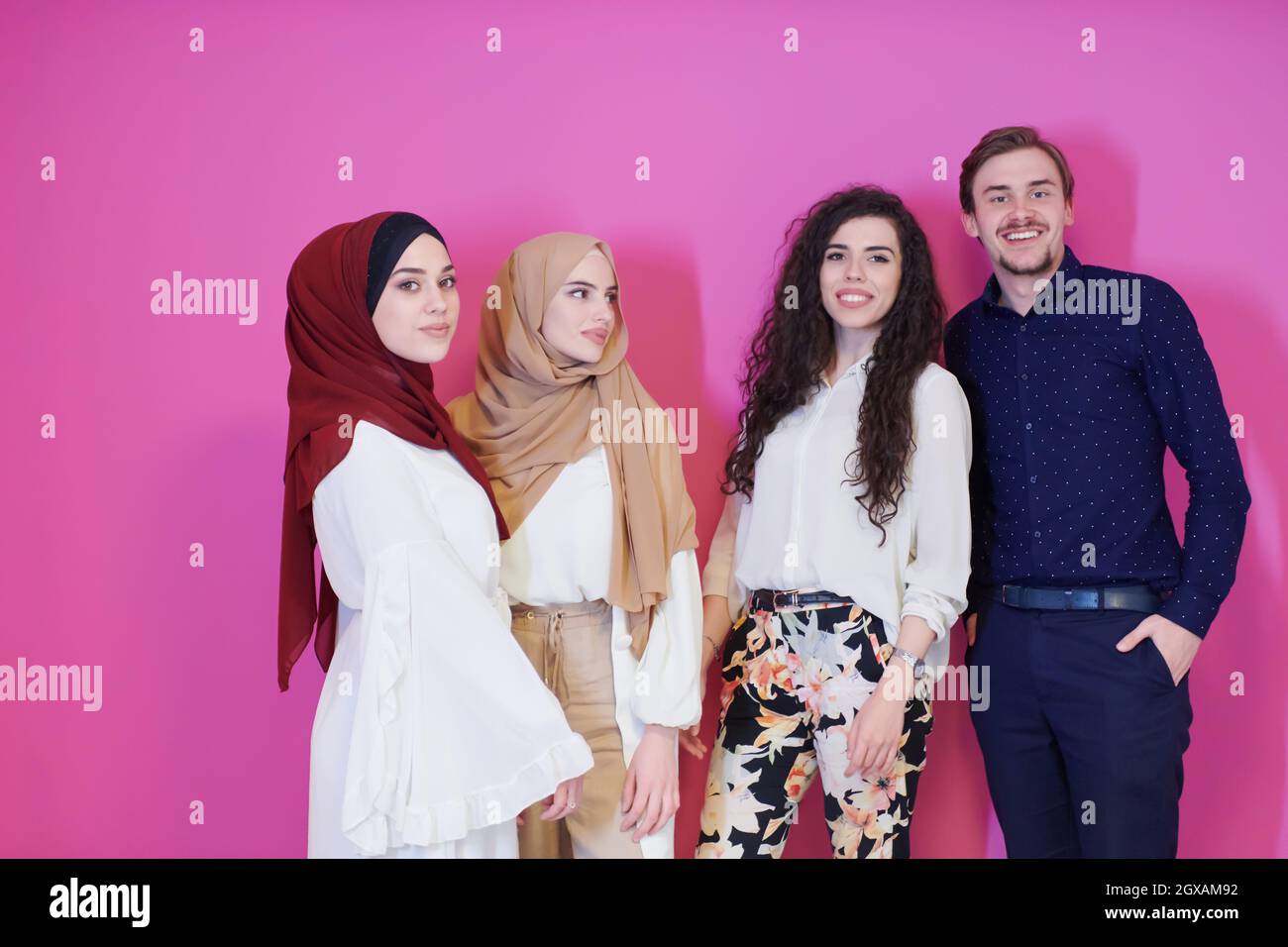 group portrait of young muslim people two of them in fashionable dress with hijab isolated on pink background representing modern islam fashion and ra Stock Photo
