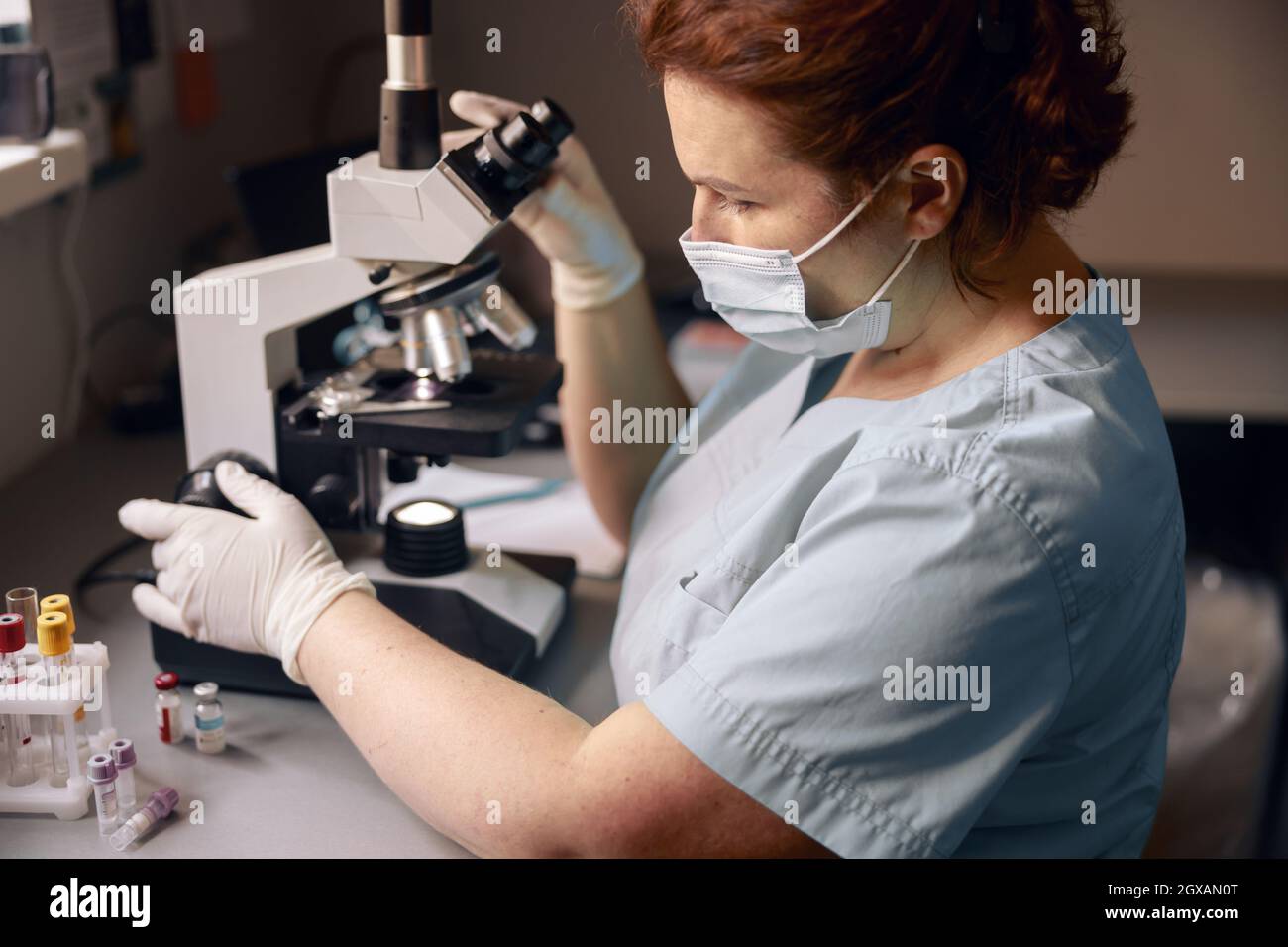 Middle aged lab technician adjusts microscope to research material ...