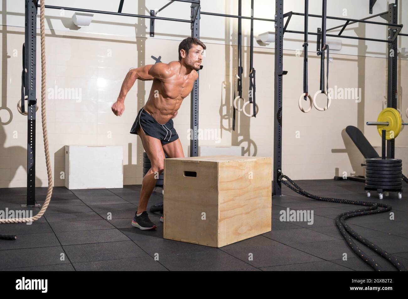 Muscular male athlete is practicing jumping on a wooden box in modern health club. Functional training. High quality photo. Stock Photo