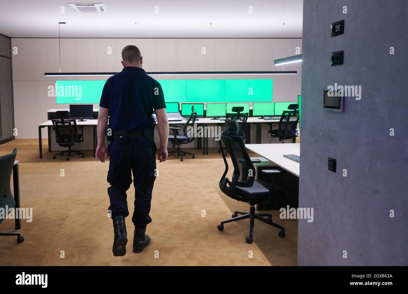 young male security operator walking through data system control room Working at workstation with multiple displays, security guard working on multipl Stock Photo