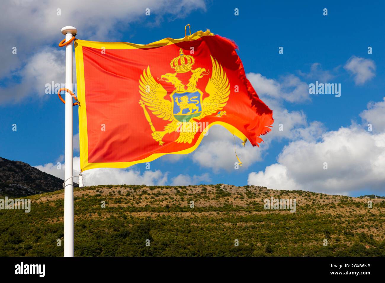 Flag of Montenegro waving in the wind with sky and mountains in background. Stock Photo