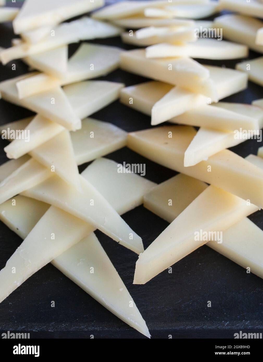 Cured slices of manchego cheese over black slate tray. Closeup. Stock Photo