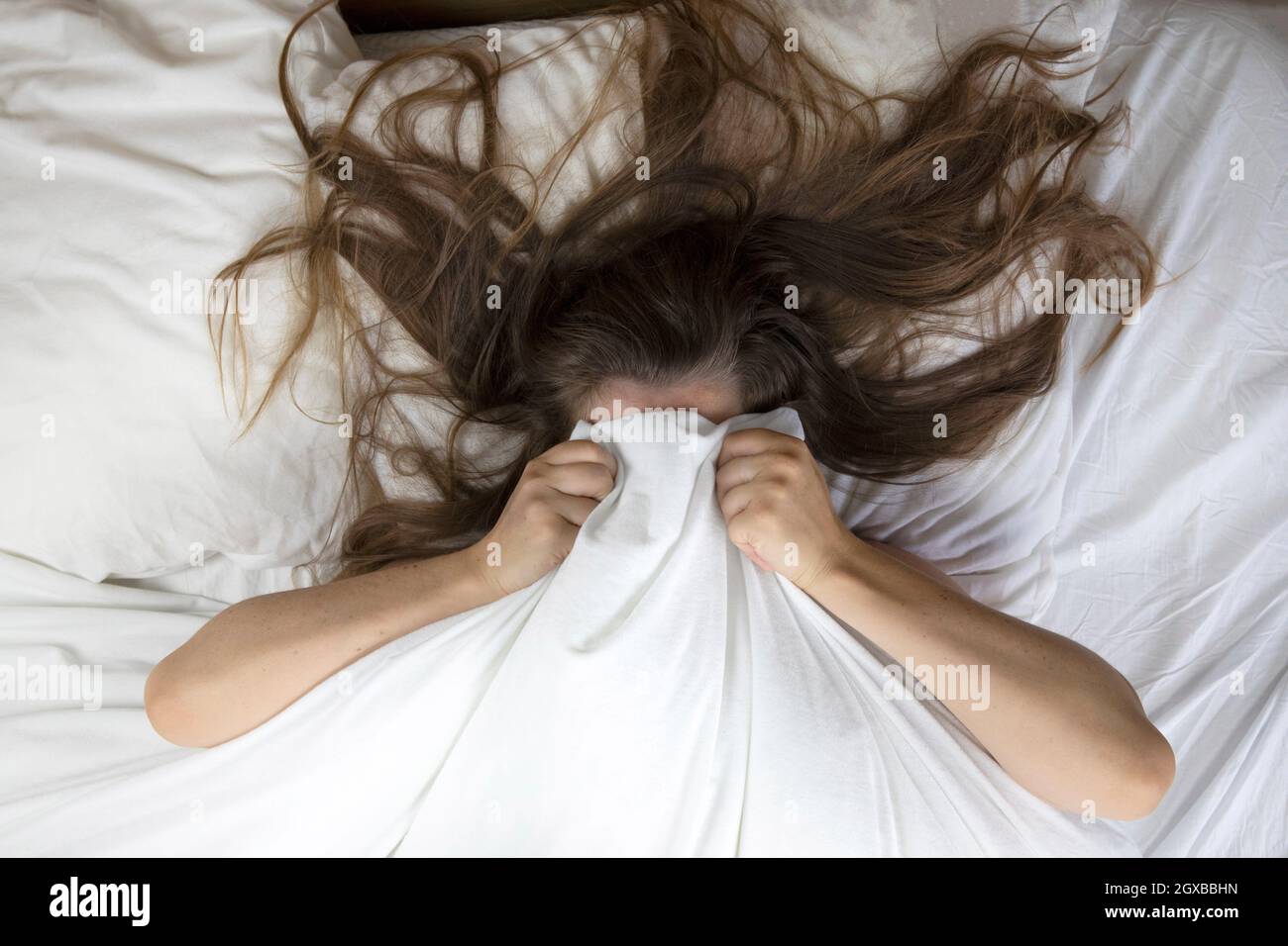 Young woman lying in bed suffering, tired woman covering face with