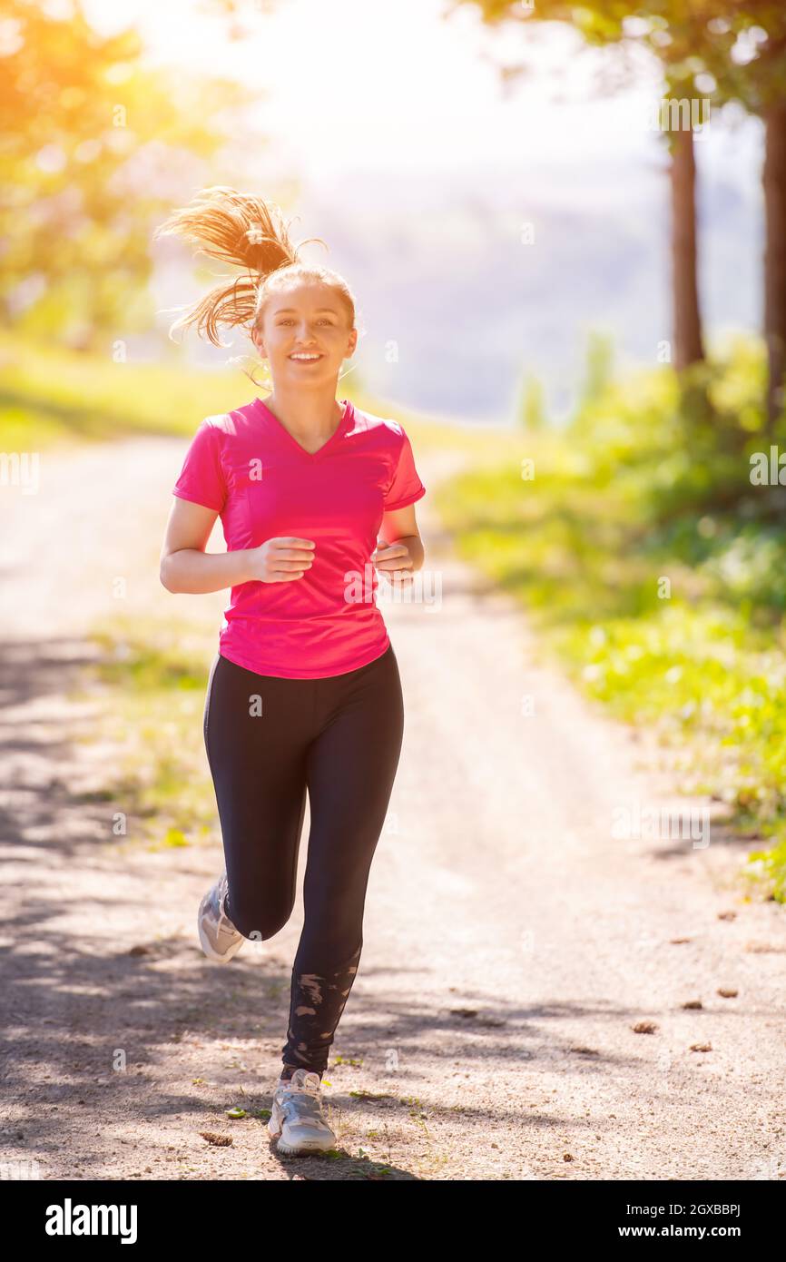 woman jogging on a country road through the beautiful sunny forest