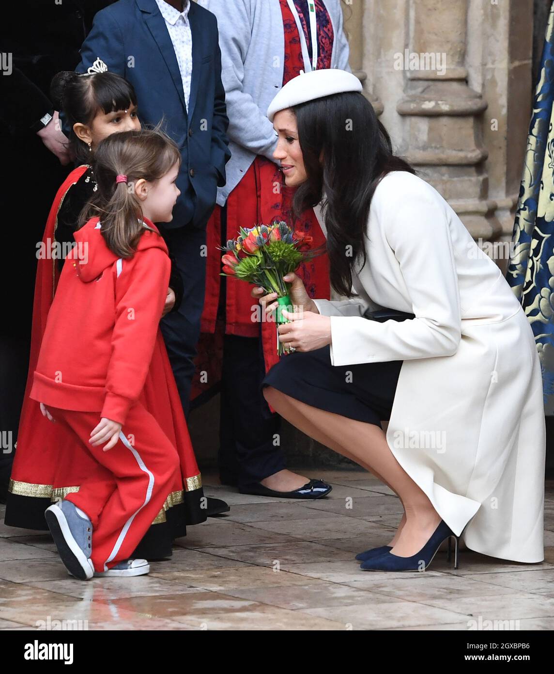 Meghan Markle, wearing a cream Amanda Wakeley coat and matching hat, receives a posy of flowers from a young girl following the Commonwealth Service at Westminster Abbey in London on March 12, 2018. Stock Photo