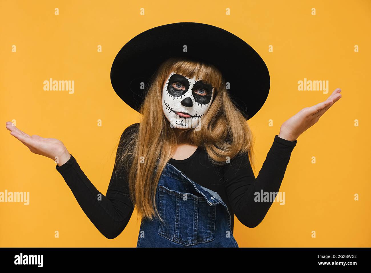 Confused girl kid with Halloween makeup mask wears big black hat