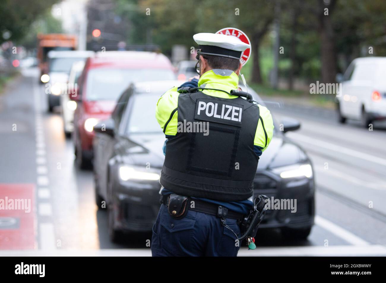 Dresden, Germany. 05th Oct, 2021. A police officer from the Dresden police  department stands in front of several vehicles with a waving trowel during  a check as part of the "Respect through